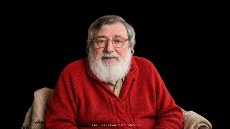 Un ritratto intenso in bianco e nero di Francesco Guccini seduto sul portico della sua casa a Pavana, circondato da una chitarra acustica e da libri, mentre guarda pensoso la telecamera