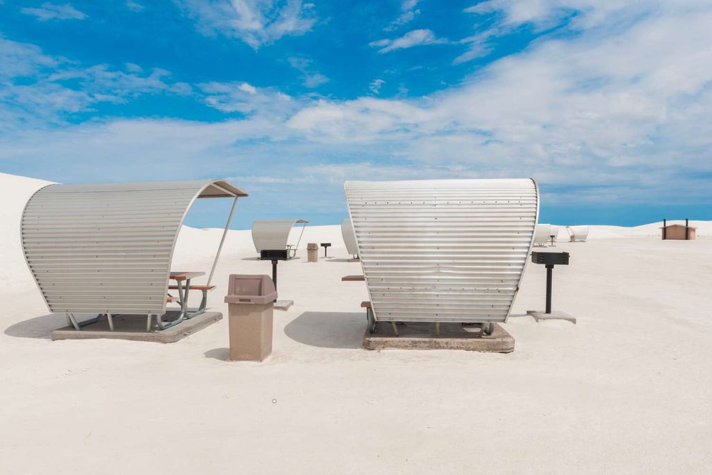 Area picnic attrezzata con tavoli coperti in metallo e griglie per barbecue integrate tra le dune di gesso candido a White Sands.