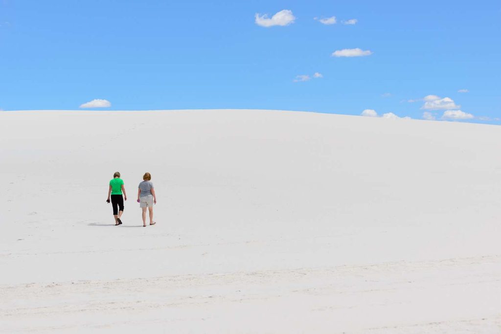 Turisti camminano in lontananza lungo una cresta di dune di gesso bianco brillante alle White Sands, risaltando contro l'azzurro intenso del cielo.