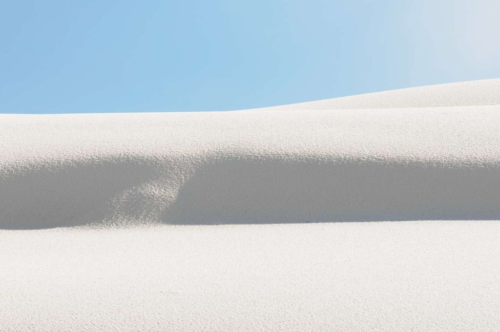 Dune e ombre: Un'immagine che cattura il contrasto netto tra la sabbia bianca e le ombre profonde create dalla curvatura della duna, in una composizione geometrica.