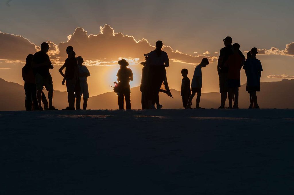Un gruppo di ranger in uniforme cammina in fila lungo la cresta di una duna bianca durante la passeggiata al tramonto a White Sands.