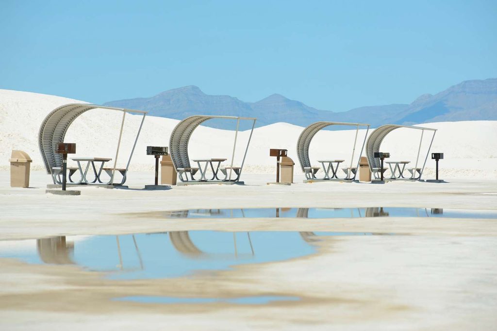 Un palcoscenico all'aperto e file di sedie per il pubblico installate direttamente sulle distese di sabbia bianca e finissima delle White Sands, circondate da montagne lontane sotto un cielo terso.